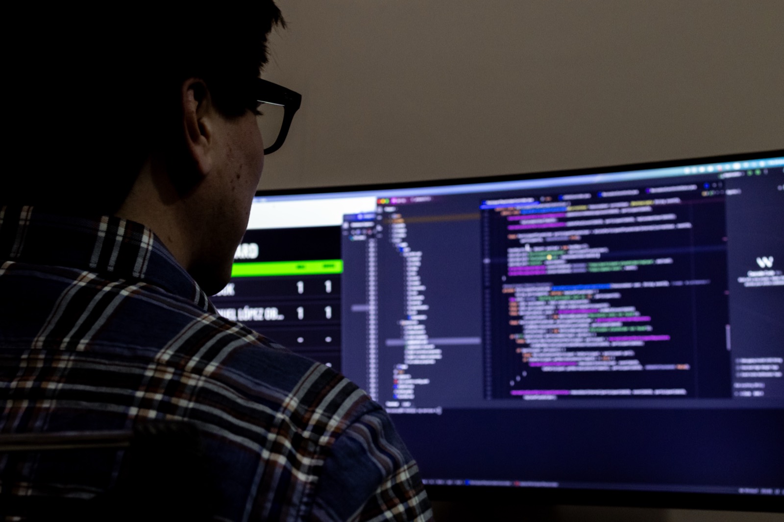A Dallio developer reviewing application code on an ultrawide monitor at the studio in México